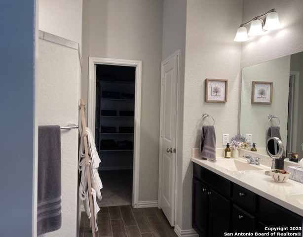 full bath with vanity, wood tiled floors, a walk in closet, and baseboards
