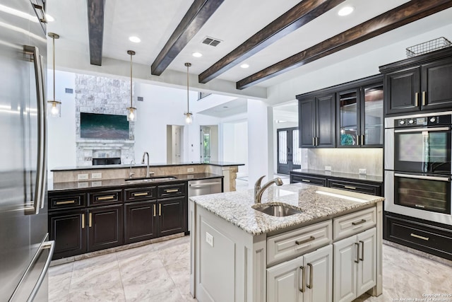 6327 Almeria Cir, San Antonio, TX 78257 - kitchen featuring appliances with stainless steel finishes, a sink, a kitchen island with sink, backsplash, and beam ceiling