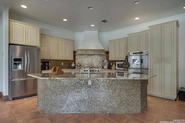 19902 Messina, San Antonio, TX 78258 - kitchen featuring cream cabinetry, appliances with stainless steel finishes, custom exhaust hood, stone counters, and a center island with sink