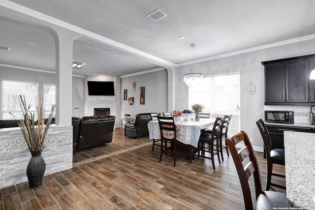 23534 Enchanted Bnd, San Antonio, TX 78260 - dining space featuring ornamental molding, healthy amount of natural light, a stone fireplace, dark wood-style floors, and a textured ceiling