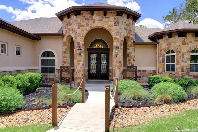 view of exterior entry with a shingled roof, stucco siding, stone siding, and french doors