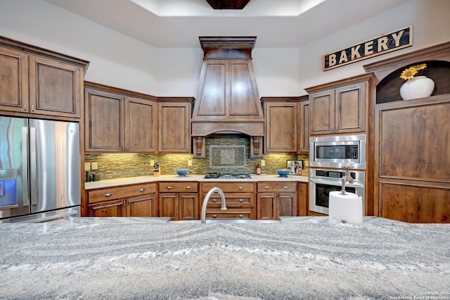kitchen with appliances with stainless steel finishes, backsplash, premium range hood, and light stone countertops