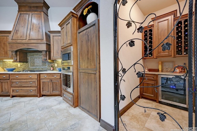 kitchen with stainless steel appliances, tasteful backsplash, brown cabinetry, custom exhaust hood, and light countertops