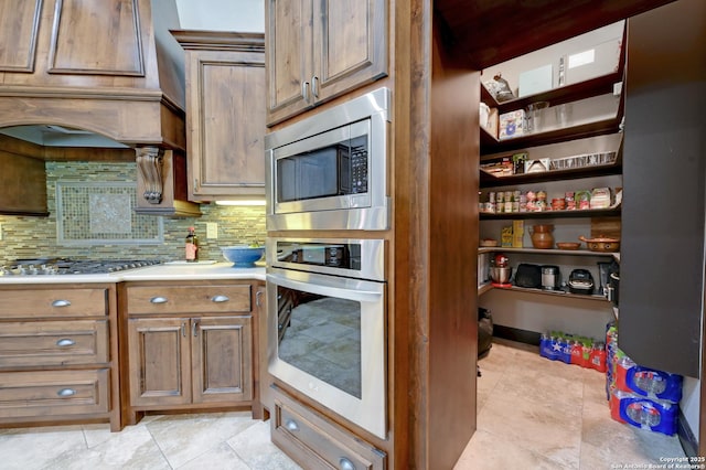 kitchen featuring appliances with stainless steel finishes, backsplash, light countertops, brown cabinets, and light tile patterned flooring