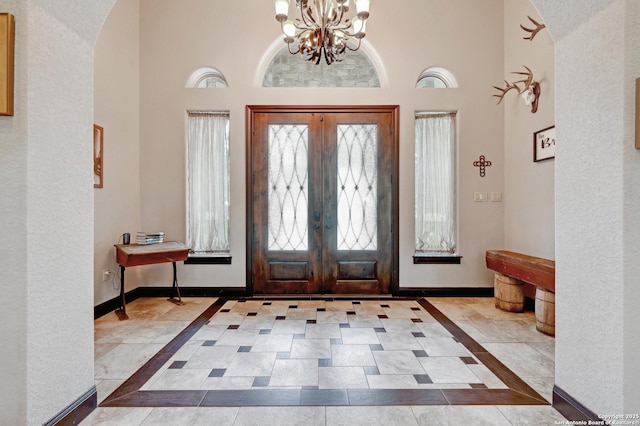 entrance foyer featuring arched walkways, a chandelier, baseboards, a high ceiling, and french doors