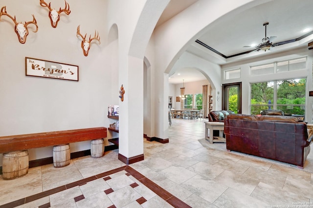 hallway featuring baseboards, arched walkways, a high ceiling, recessed lighting, and a tray ceiling