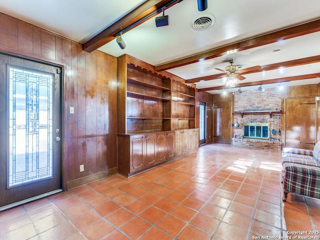 355 Donella, Hollywood Park, TX 78232 - unfurnished living room featuring beam ceiling, wooden walls, ceiling fan, a brick fireplace, and tile patterned floors