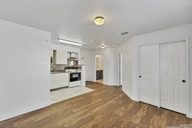 11219 Five Iron, San Antonio, TX 78221 - kitchen with white range with electric stovetop, wall chimney exhaust hood, white cabinetry, wood finished floors, and baseboards