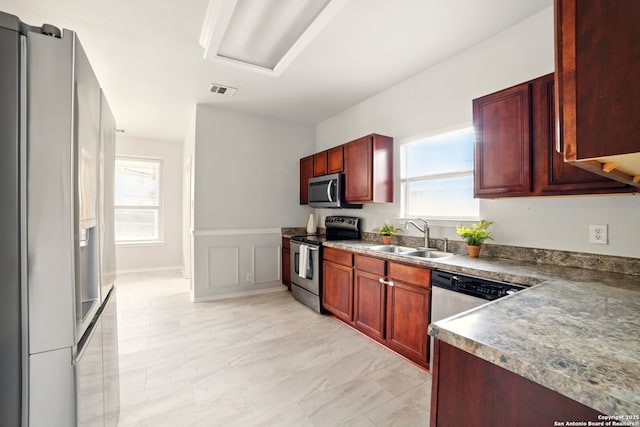 16910 Graham Walk, San Antonio, TX 78247 - kitchen with stainless steel appliances, a sink, reddish brown cabinets, healthy amount of natural light, and a wainscoted wall