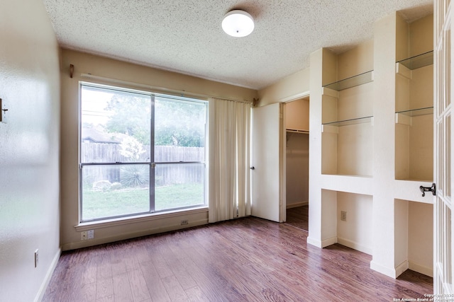 8763 Silent Oaks, San Antonio, TX 78250 - unfurnished bedroom featuring a textured ceiling, multiple windows, wood finished floors, and baseboards