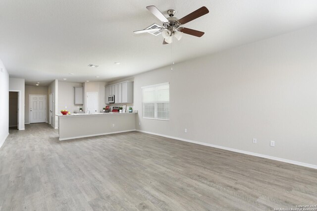 14647 Stirrup Trce, Elmendorf, TX 78112 - unfurnished living room featuring light wood finished floors, a ceiling fan, and baseboards