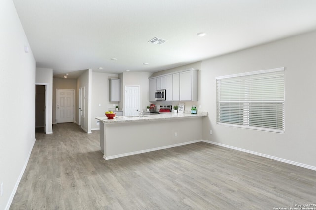 14647 Stirrup Trce, Elmendorf, TX 78112 - kitchen with appliances with stainless steel finishes, light wood-style flooring, a sink, a peninsula, and baseboards