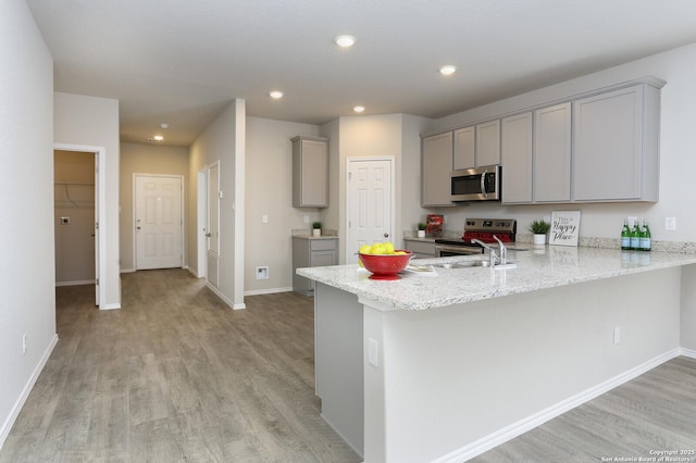14647 Stirrup Trce, Elmendorf, TX 78112 - kitchen with gray cabinetry, appliances with stainless steel finishes, light wood-type flooring, a peninsula, and light stone counters