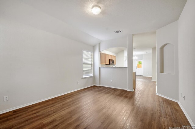 10374 Oakwood Crst, San Antonio, TX 78245 - unfurnished living room with dark wood-style flooring, baseboards, arched walkways, a chandelier, and vaulted ceiling