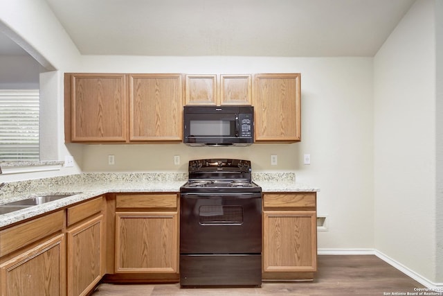 10374 Oakwood Crst, San Antonio, TX 78245 - kitchen with black appliances, wood finished floors, a sink, baseboards, and light stone counters