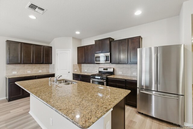 15206 Field Sparrow, San Antonio, TX 78253 - kitchen featuring stainless steel appliances, a sink, light wood-style flooring, dark brown cabinetry, and a kitchen island with sink