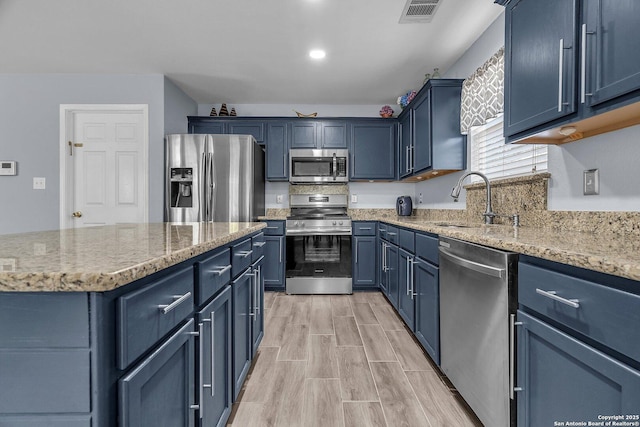7715 Beechnut Oak, San Antonio, TX 78223 - kitchen with stainless steel appliances, blue cabinets, a sink, light stone counters, and light wood-style flooring