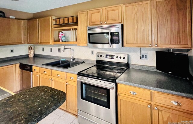 9208 Bowen, San Antonio, TX 78250 - kitchen featuring appliances with stainless steel finishes, a sink, light tile patterned floors, dark countertops, and backsplash