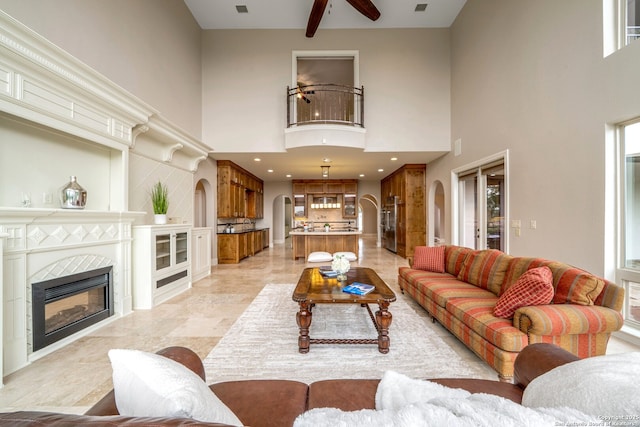 19223 Terra Rock, San Antonio, TX 78255 - living room with arched walkways, a high ceiling, a ceiling fan, a tiled fireplace, and recessed lighting
