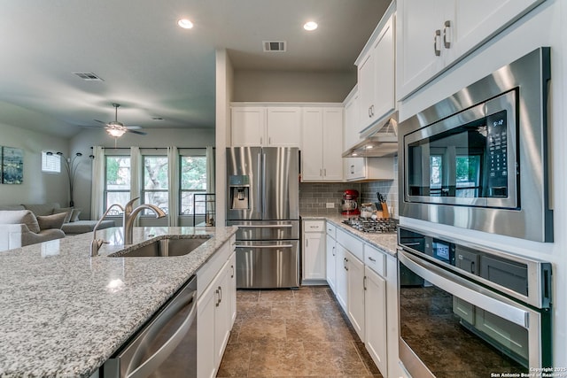 10250 Bricewood Pl, San Antonio, TX 78254 - kitchen with stainless steel appliances, a sink, under cabinet range hood, backsplash, and white cabinets