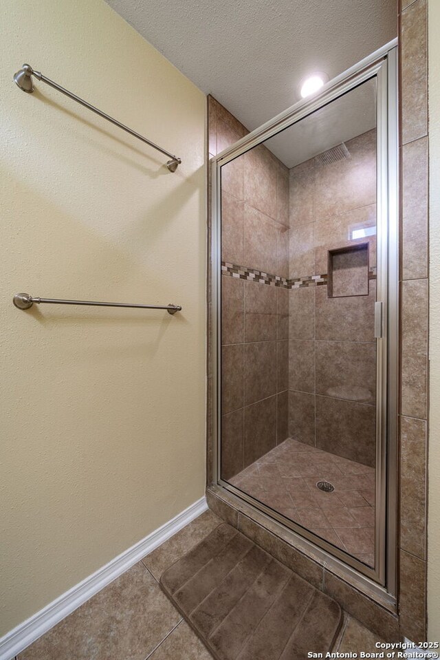 11301 Ford, Adkins, TX 78101 - bathroom featuring tile patterned floors, a stall shower, baseboards, and a textured ceiling