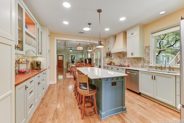 207 Queen Anne, San Antonio, TX 78209 - kitchen featuring stainless steel appliances, a sink, custom range hood, light wood-style floors, and a kitchen island