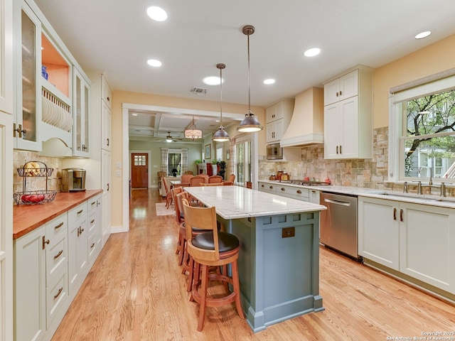 207 Queen Anne, San Antonio, TX 78209 - kitchen with stainless steel appliances, premium range hood, a kitchen island, a sink, and light wood-style flooring
