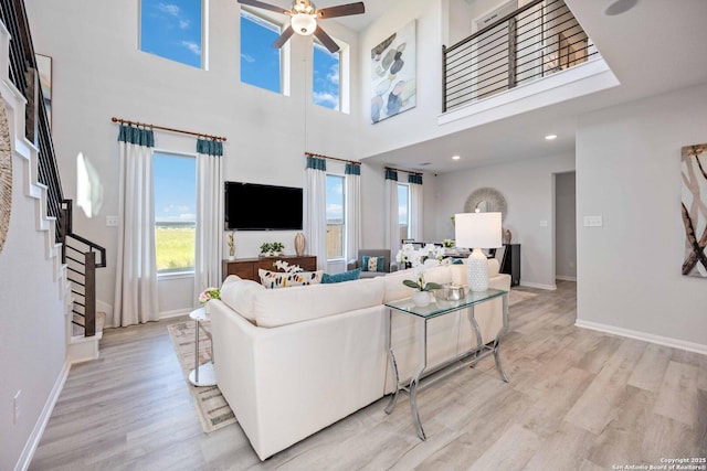 8644 Merlin Cv, San Antonio, TX 78222 - living room with light wood-style flooring, a ceiling fan, baseboards, a high ceiling, and stairs