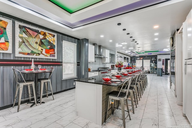 1002 Alpine Pond, San Antonio, TX 78260 - kitchen featuring light marble finish floors, a breakfast bar, dark countertops, wall chimney exhaust hood, and recessed lighting