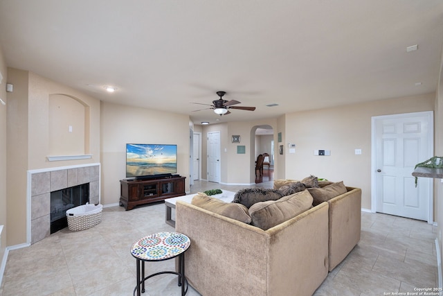 11106 Shetland Hls, San Antonio, TX 78254 - living room featuring arched walkways, a ceiling fan, baseboards, a tiled fireplace, and light tile patterned flooring