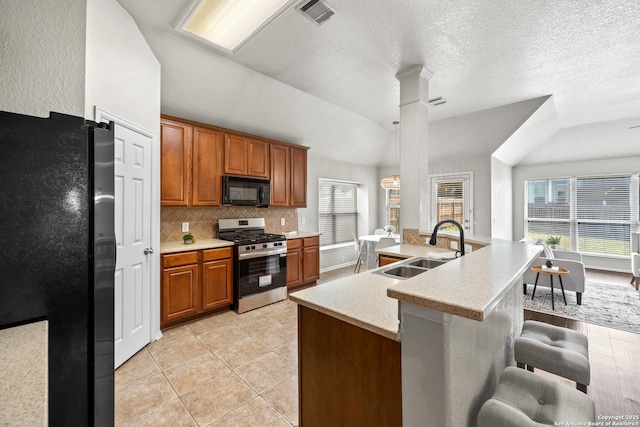 26430 Walden Oak, San Antonio, TX 78260 - kitchen with freestanding refrigerator, stainless steel range with gas cooktop, black microwave, a sink, and a breakfast bar