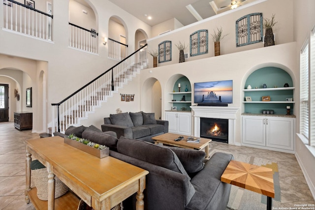 17906 Via Del Arbol, San Antonio, TX 78257 - living room featuring a towering ceiling, built in shelves, a glass covered fireplace, baseboards, and stairs
