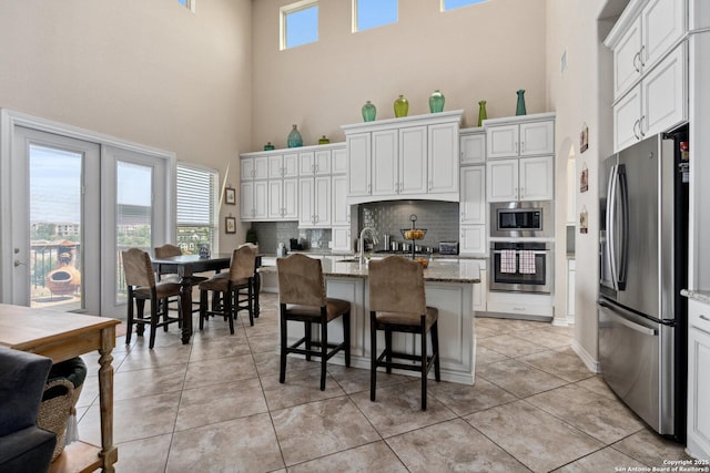 17906 Via Del Arbol, San Antonio, TX 78257 - kitchen with stainless steel appliances, a towering ceiling, backsplash, light stone countertops, and a center island with sink