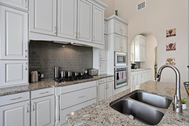 17906 Via Del Arbol, San Antonio, TX 78257 - kitchen featuring appliances with stainless steel finishes, a sink, arched walkways, white cabinetry, and backsplash