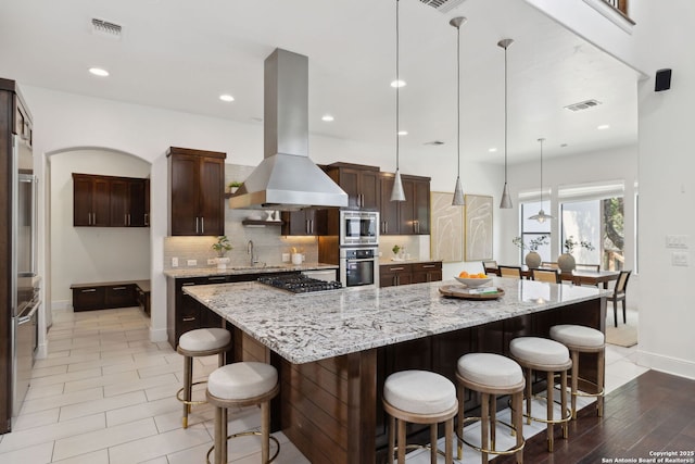 17706 Wild Basin, San Antonio, TX 78258 - kitchen featuring appliances with stainless steel finishes, island exhaust hood, baseboards, backsplash, and a breakfast bar area