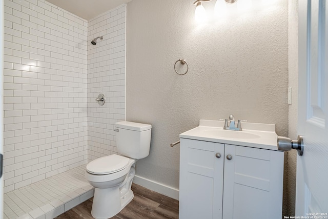 2411 W Huisache Ave, San Antonio, TX 78228 - bathroom with toilet, a tile shower, wood finished floors, vanity, and baseboards