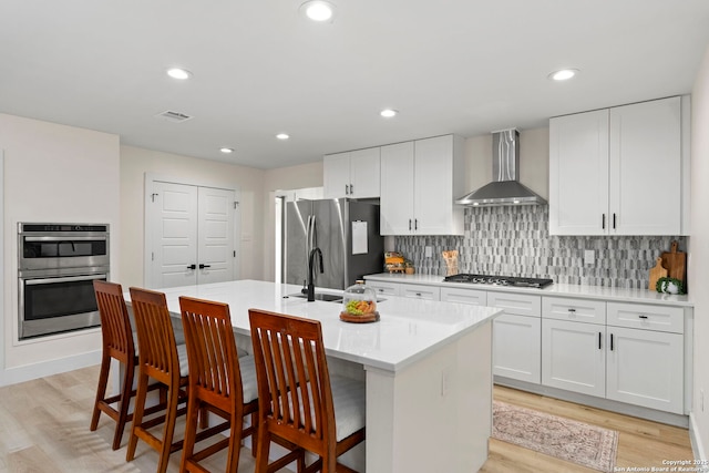 500 Skyforest, Hollywood Park, TX 78232 - kitchen featuring wall chimney exhaust hood, stainless steel appliances, light wood-type flooring, an island with sink, and decorative backsplash