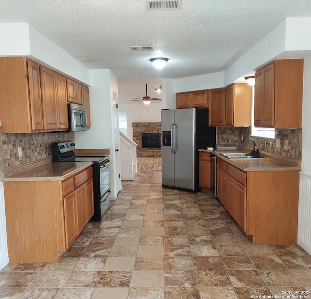 3730 Candlestone, San Antonio, TX 78244 - kitchen featuring appliances with stainless steel finishes, a sink, a fireplace, decorative backsplash, and a ceiling fan