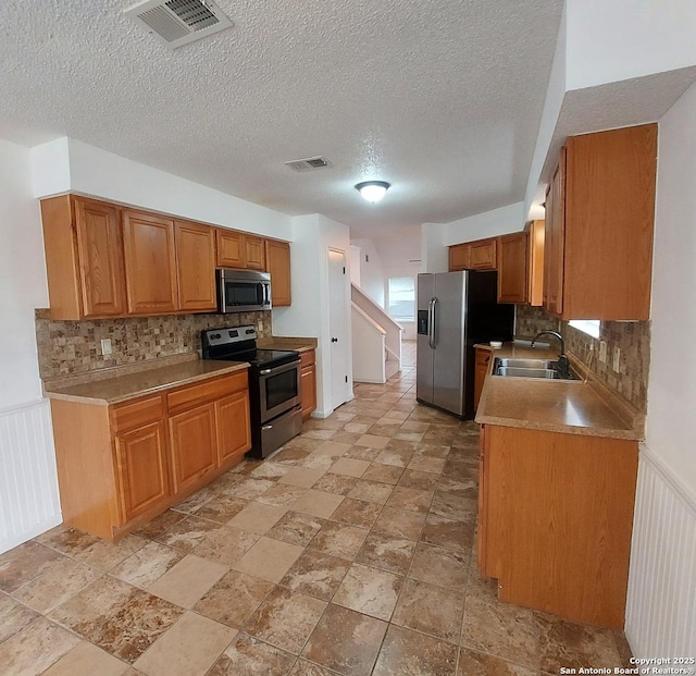 3730 Candlestone, San Antonio, TX 78244 - kitchen featuring appliances with stainless steel finishes, a sink, backsplash, a textured ceiling, and light stone finish floors
