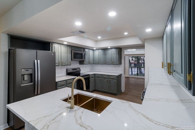 9215 Standing Crk, San Antonio, TX 78230 - kitchen with stainless steel appliances, a sink, gray cabinetry, a tray ceiling, and light stone countertops