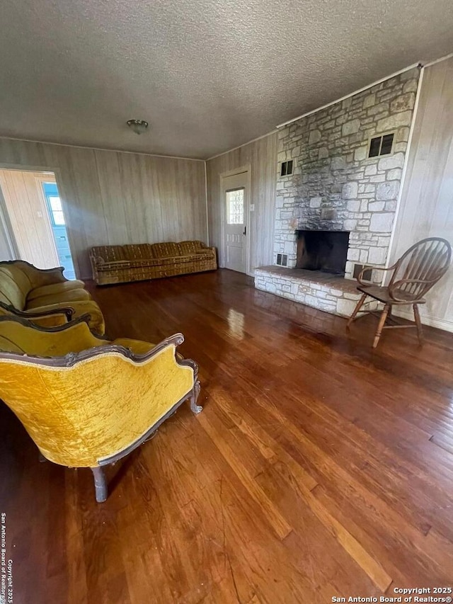 8439 Gardner, San Antonio, TX 78263 - living room featuring a textured ceiling, wood finished floors, a stone fireplace, and wooden walls