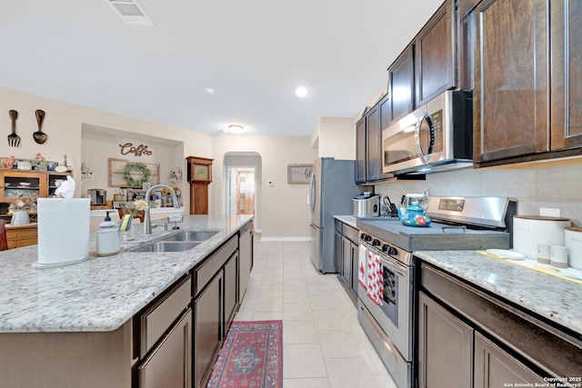 5903 Overture Dawn, San Antonio, TX 78252 - kitchen with appliances with stainless steel finishes, a sink, arched walkways, dark brown cabinetry, and a kitchen island with sink