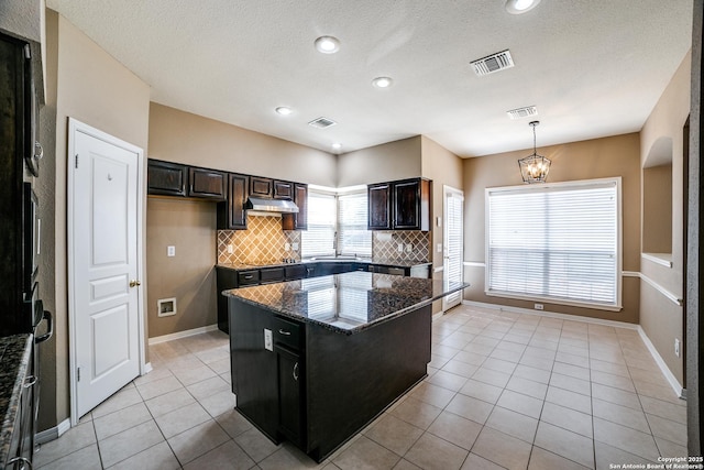 5018 Ashton Audrey, San Antonio, TX 78249 - kitchen with under cabinet range hood, tasteful backsplash, light tile patterned floors, baseboards, and a kitchen island