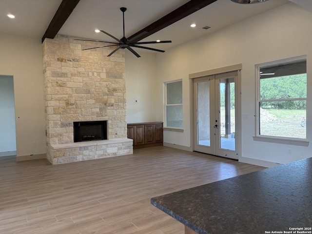 811 Horseshoe Fls, Bandera, TX 78003 - unfurnished living room featuring beamed ceiling, a ceiling fan, light wood-style floors, french doors, and a stone fireplace