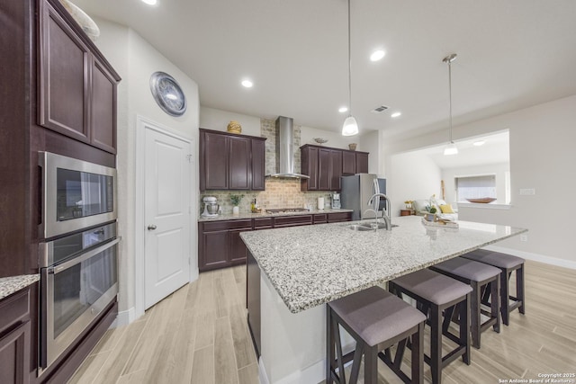 12322 Saddle Up Dr, San Antonio, TX 78254 - kitchen featuring wall chimney exhaust hood, appliances with stainless steel finishes, a sink, light wood finished floors, and a kitchen breakfast bar