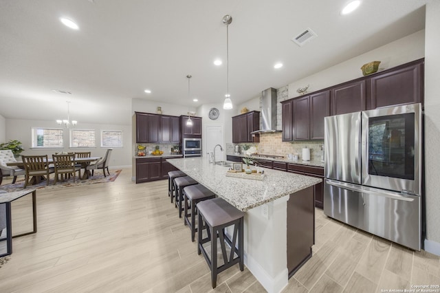 12322 Saddle Up Dr, San Antonio, TX 78254 - kitchen featuring appliances with stainless steel finishes, wall chimney range hood, a breakfast bar, light wood finished floors, and recessed lighting