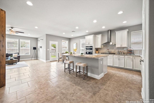 10218 Nate Range, San Antonio, TX 78254 - kitchen featuring wall chimney exhaust hood, stainless steel appliances, recessed lighting, a center island with sink, and white cabinets