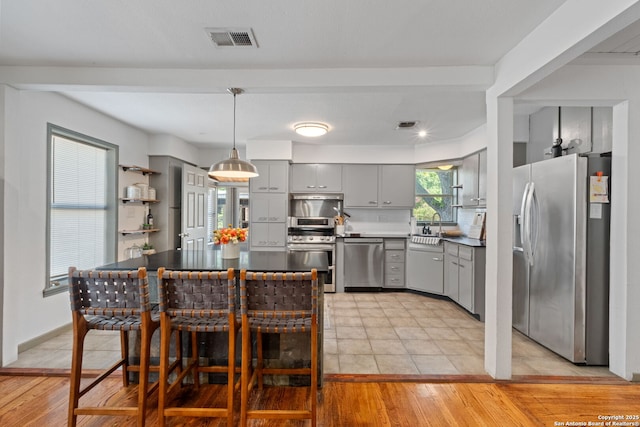 221 Calumet, San Antonio, TX 78209 - kitchen featuring stainless steel appliances, gray cabinetry, a sink, decorative light fixtures, and light wood finished floors
