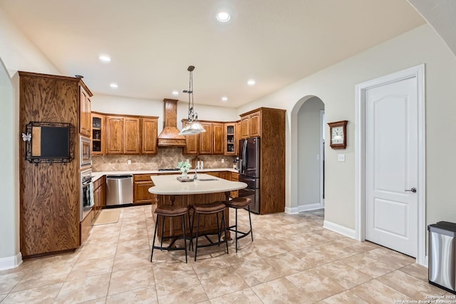 12424 Andice, Helotes, TX 78023 - kitchen featuring custom exhaust hood, arched walkways, stainless steel appliances, brown cabinets, and backsplash