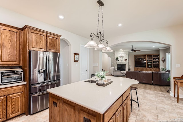 12424 Andice, Helotes, TX 78023 - kitchen with stainless steel fridge, arched walkways, a ceiling fan, a center island with sink, and brown cabinets
